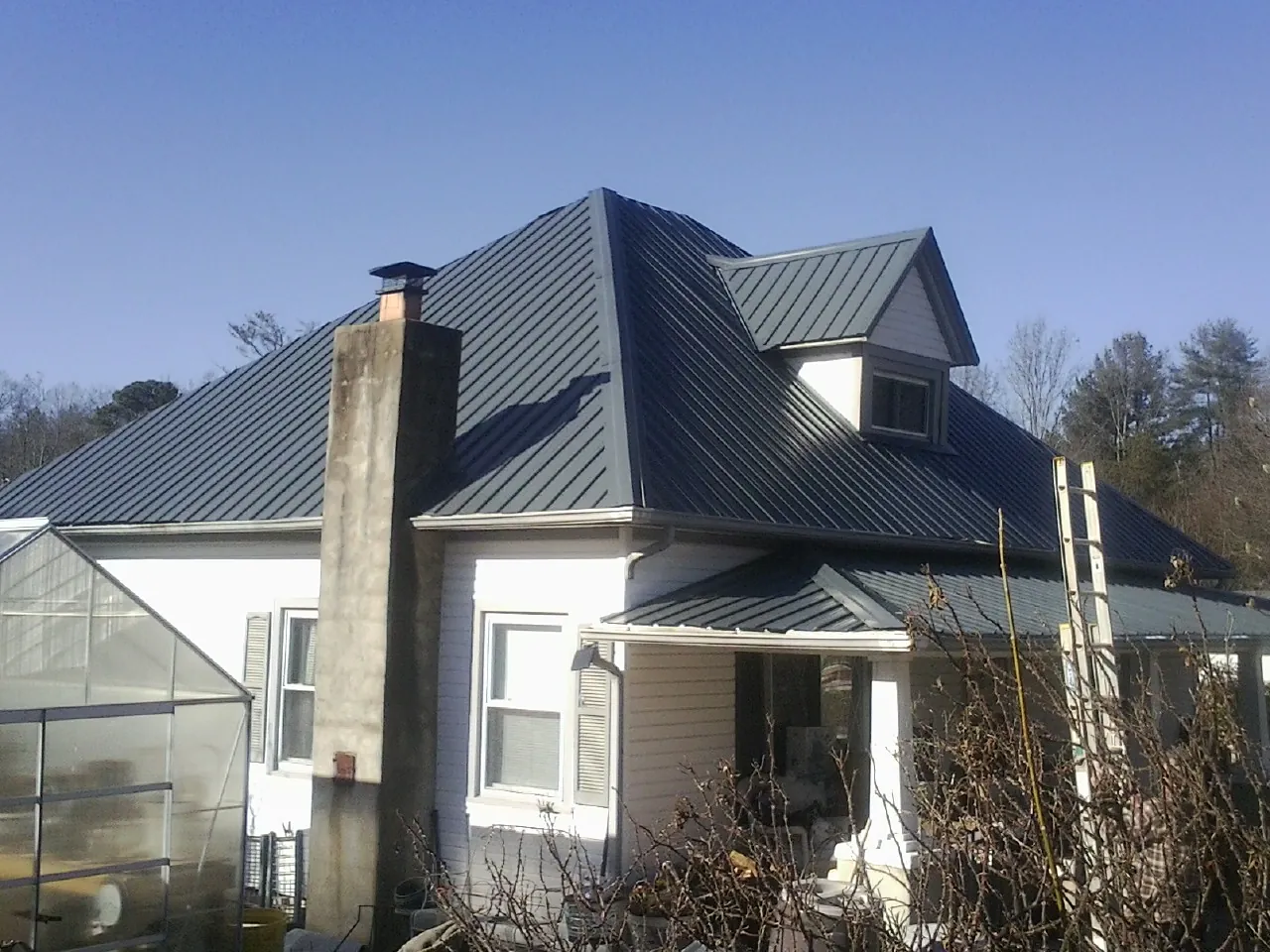 Dark blue standing seam metal roof on a white farmhouse with dormer — Slate & Tile Roof Repair by Roofing Brothers in Alderson
