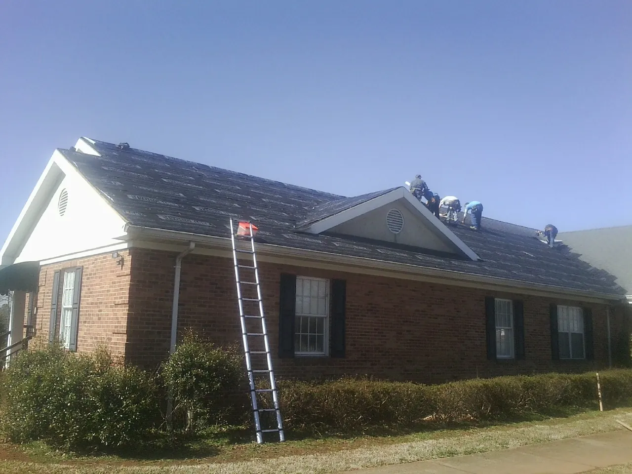 Crew tearing shingles off a brick ranch roof with a ladder set — Emergency Roof Repair work by our crew in Alderson