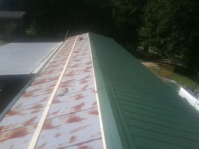 Old rusted panels beside newly installed green metal roofing — Wind Damage Roof Repair by Roofing Brothers in Alderson