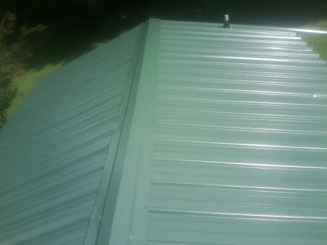 New green metal panels meeting at the ridge of a roof — Flat Roof Repair work by our crew in Alderson