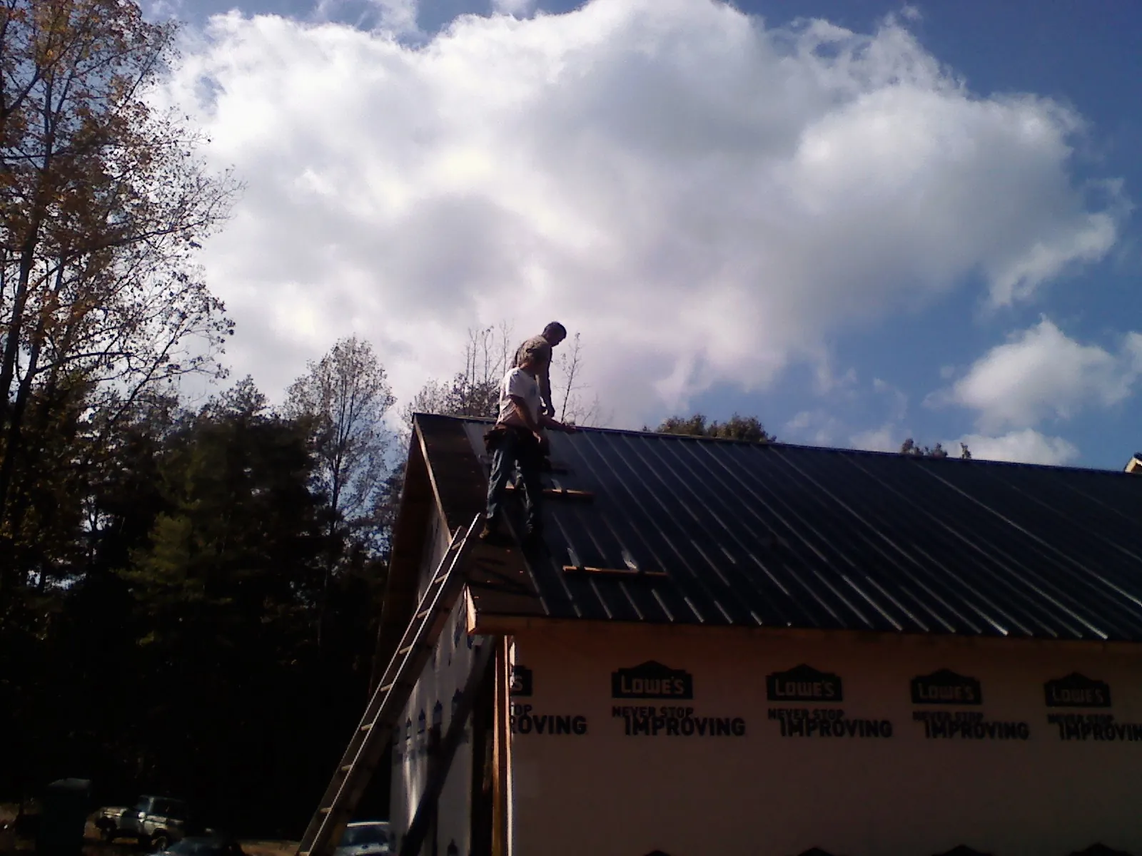 Roofer fastening dark metal panels high against a cloudy sky, from a Roof Inspection job in Alderson