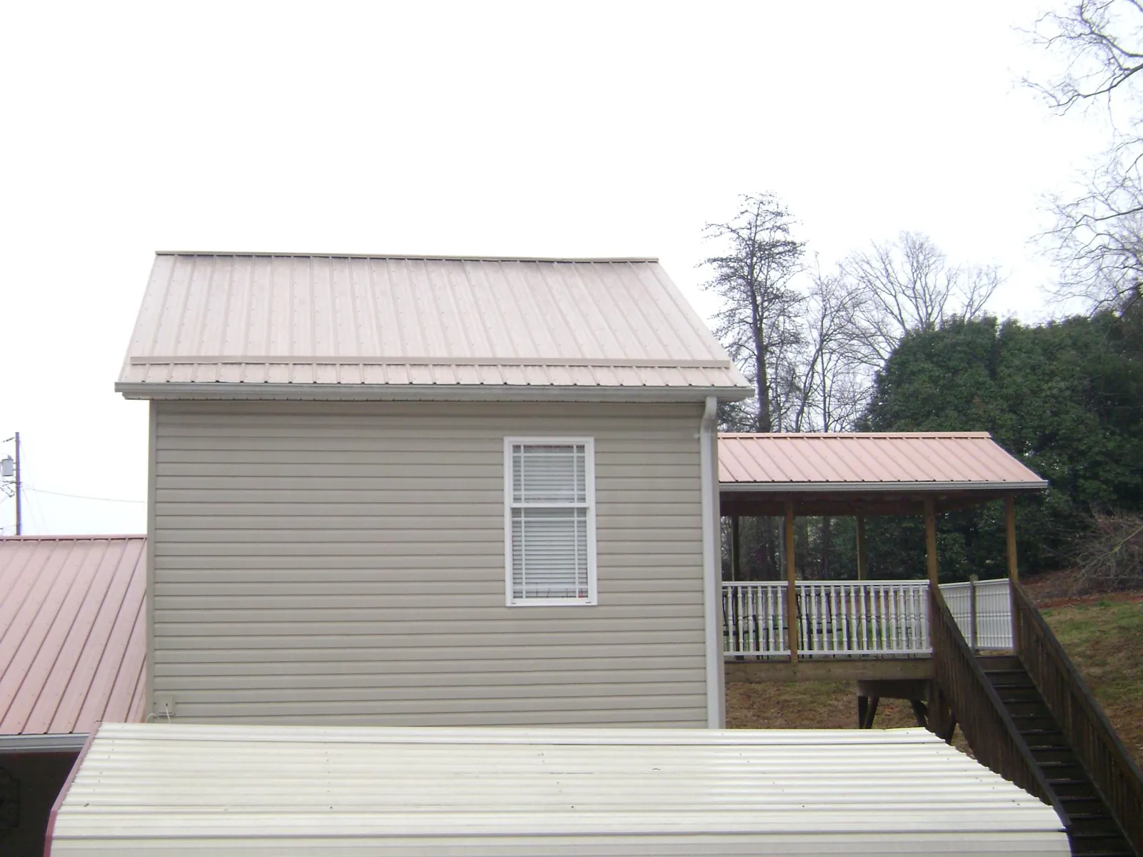 Tan metal roofs on a two story addition and attached porch, from a Roof Replacement job in Alderson